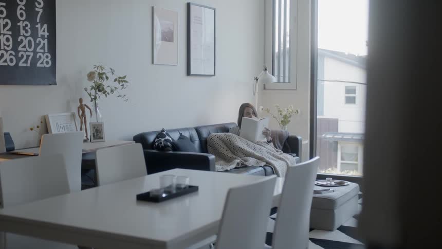 Woman sits on a couch covered with a blanket reading a book