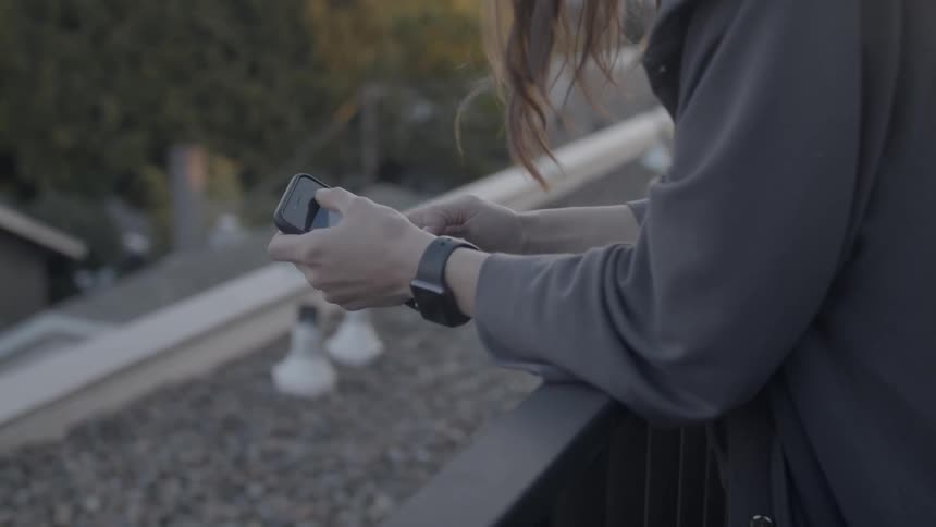 Woman leans over a balcony railing looking at a phone