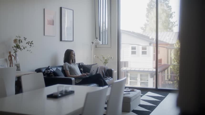 Woman sits on a sofa as she types on a laptop