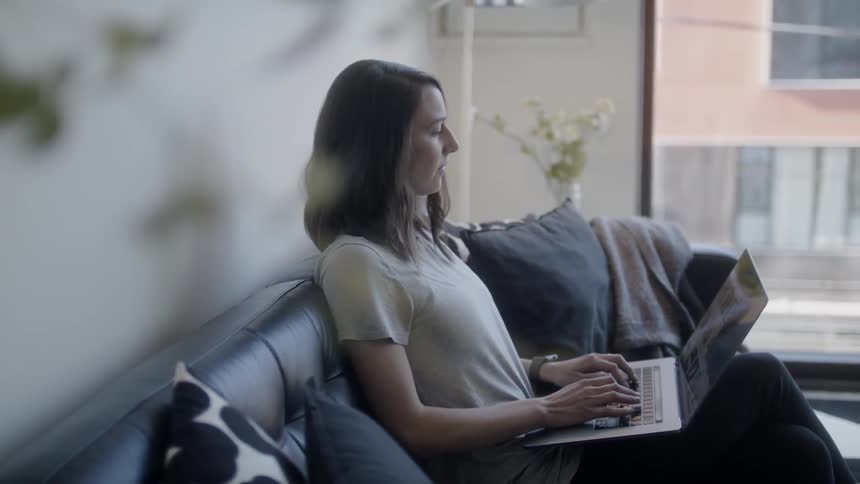 Woman sits on a couch typing on a laptop