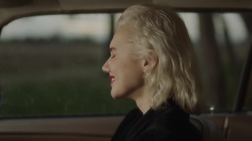 A woman is closing her eyes and laughing as she sits inside a car in daylight
