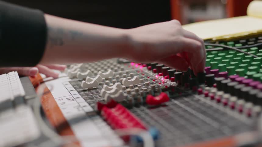 A music engineer adjusts knobs on a mixing board