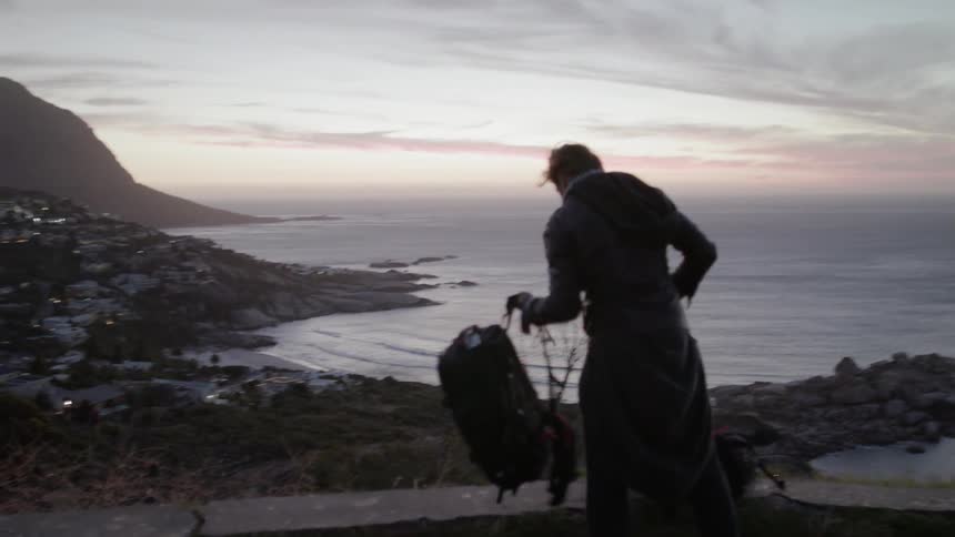 A man drops his backpack atop the cliff overlooking the town