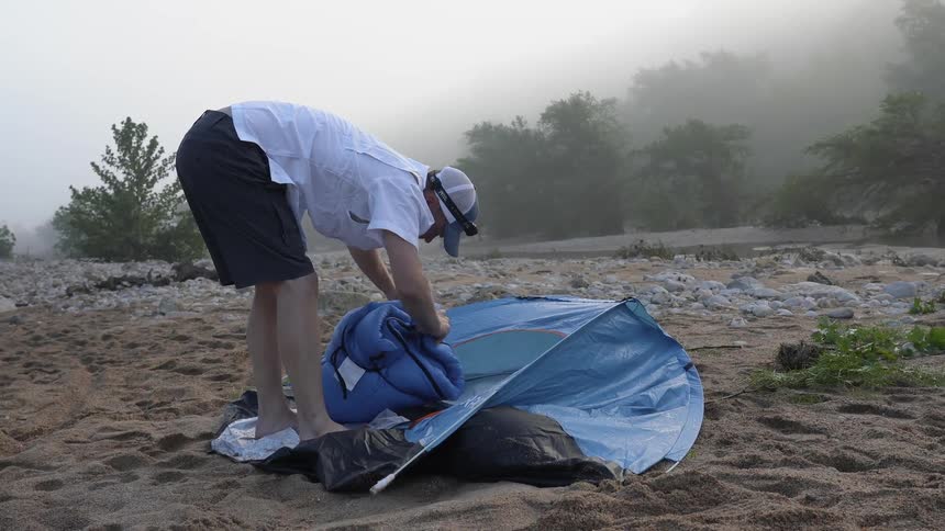 Man wraps up a sleeping bag on a sandy ground