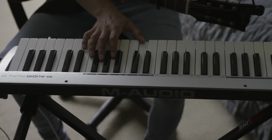 A man holding a guitar plays a keyboard