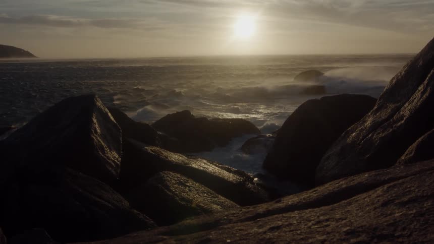 Waves crash over the rocks under the setting sun