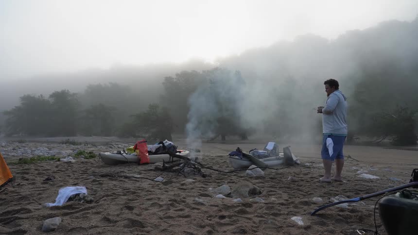 Smoke billows up from a fireplace in a campsite near a kayak