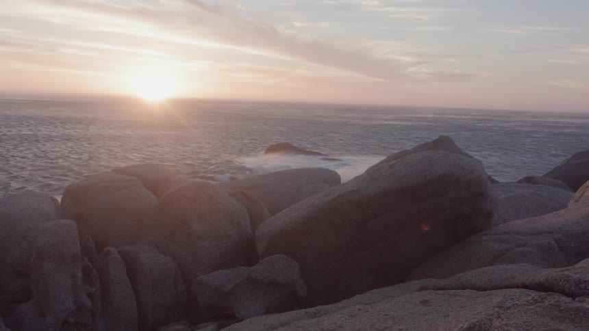 Ocean waves crash towards the rocks under the bright sun