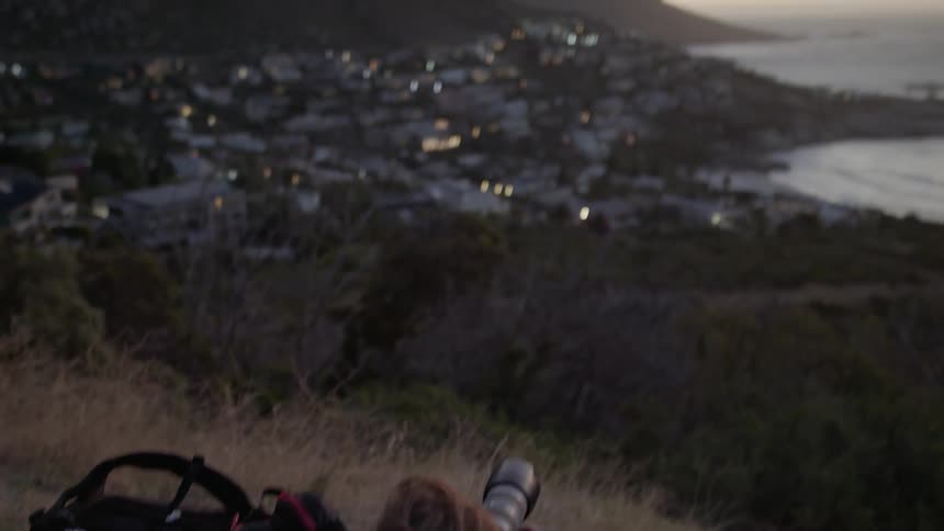 Person laying down on a hilltop taking a picture of the city below