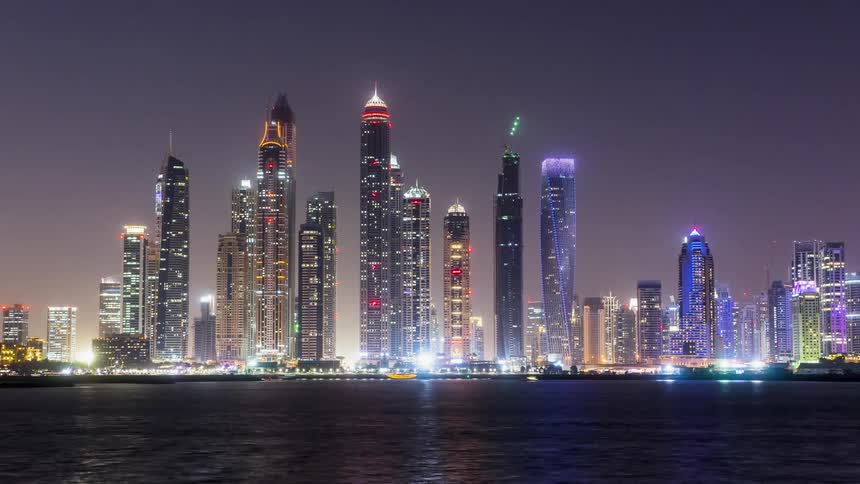 Tall illuminated buildings sit in the city as vehicles drive by