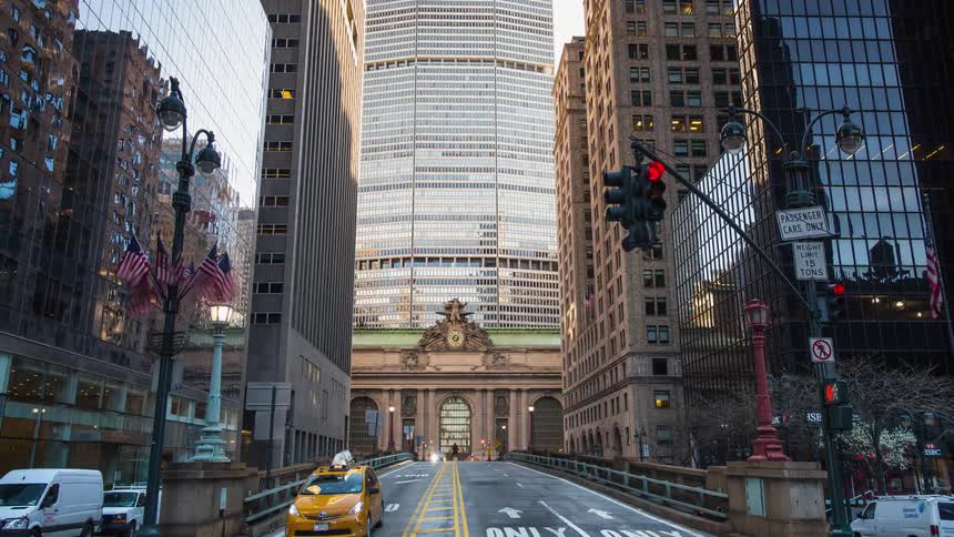 Cars drive down a busy city street next to skyscrapers