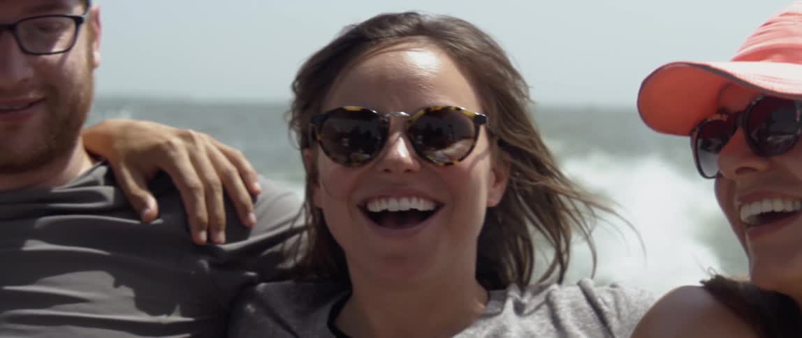 A woman is smiling and dancing as she rides in a boat on a sunny day