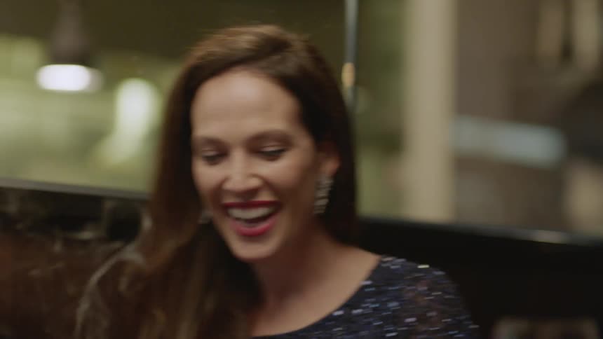 A woman celebrating her birthday with friends claps and laughs as she blows out the candles