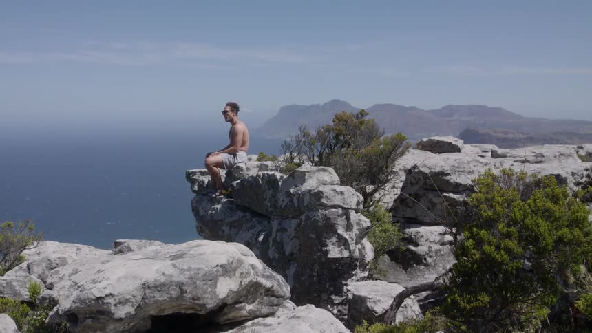 Man sits on the edge of the rocks as he looks out over the ocean