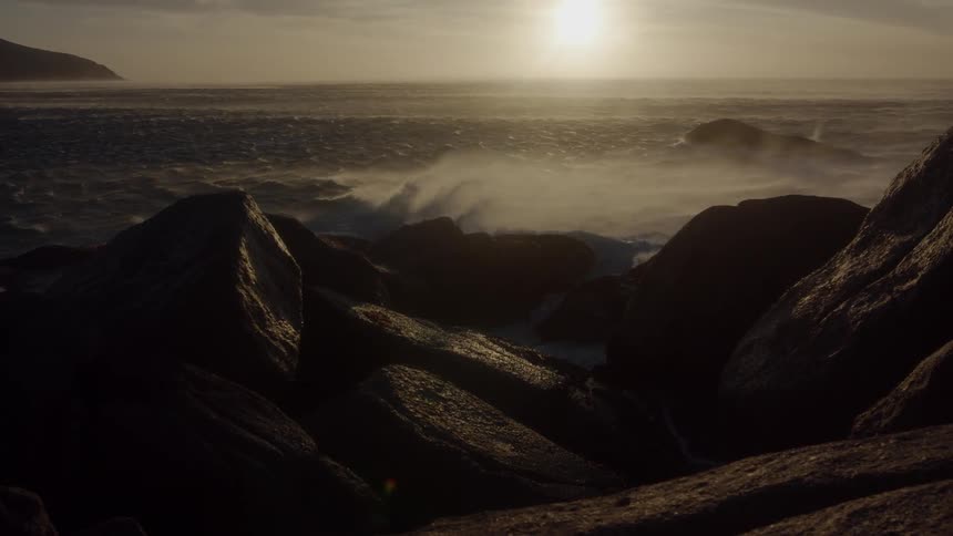 Sun shines over water misting over rocks on the beach
