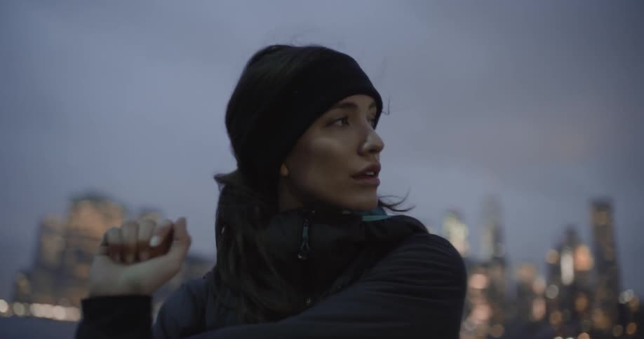 A woman stretches in front of the city at sunset