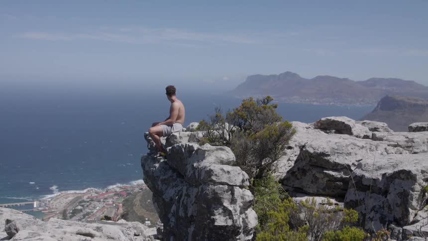 Man sits at the edge of a rocky cliff overlooking a large body of water