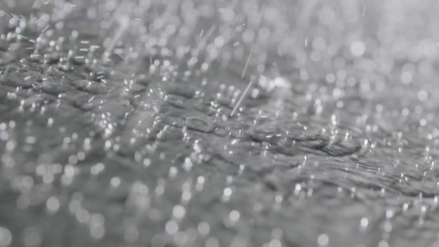 Droplets of water are raining down on a surface and flowing away
