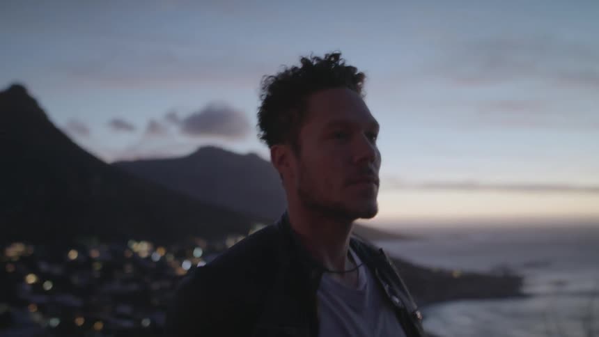 Man stands on a hilltop over a city at sunset