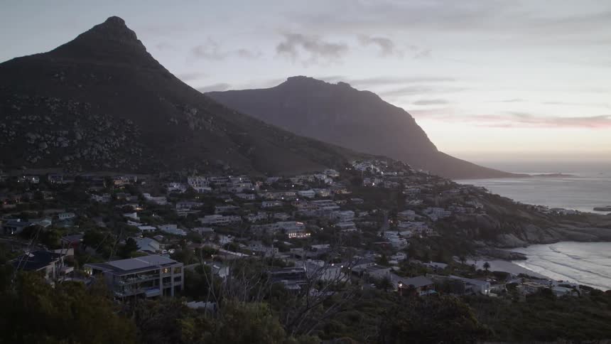 Waves roll into shore near a city at the base of a mountain