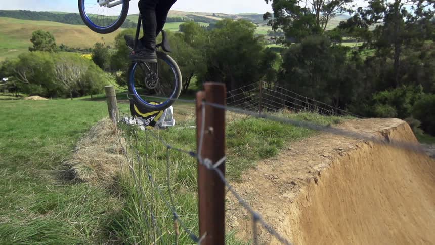 Man jumps up a dirt hill over a fence on his bike