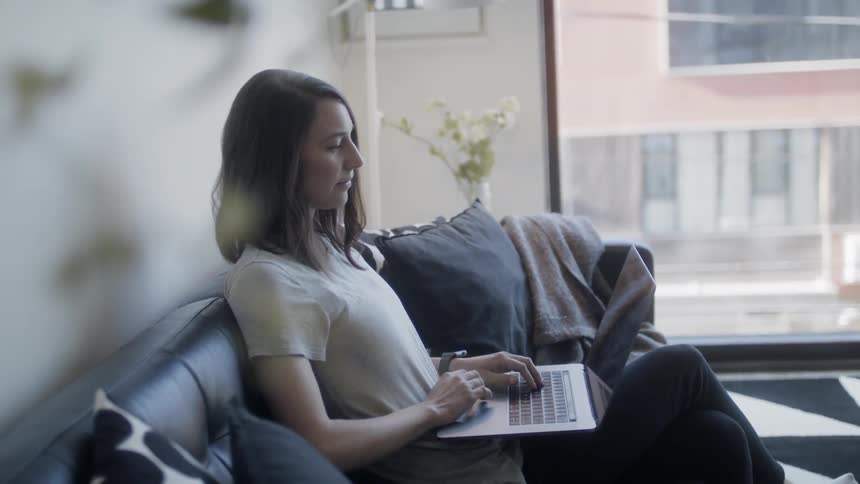 Woman sits on a couch typing on a laptop