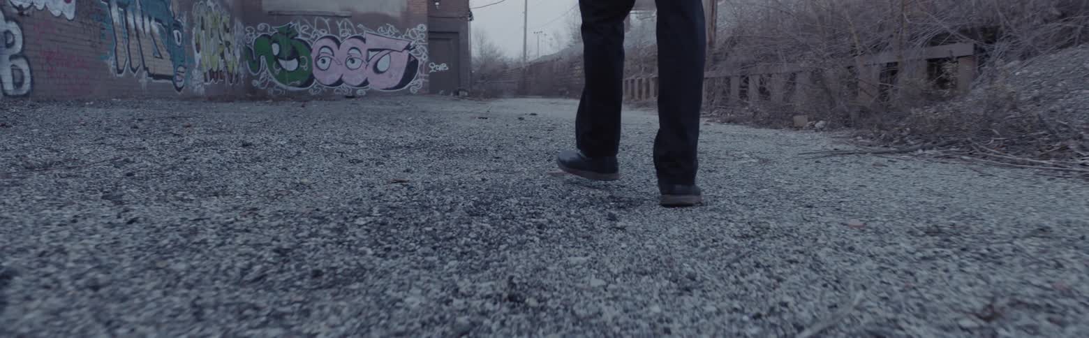 A man is walking outside a graffiti-covered building on an overcast day
