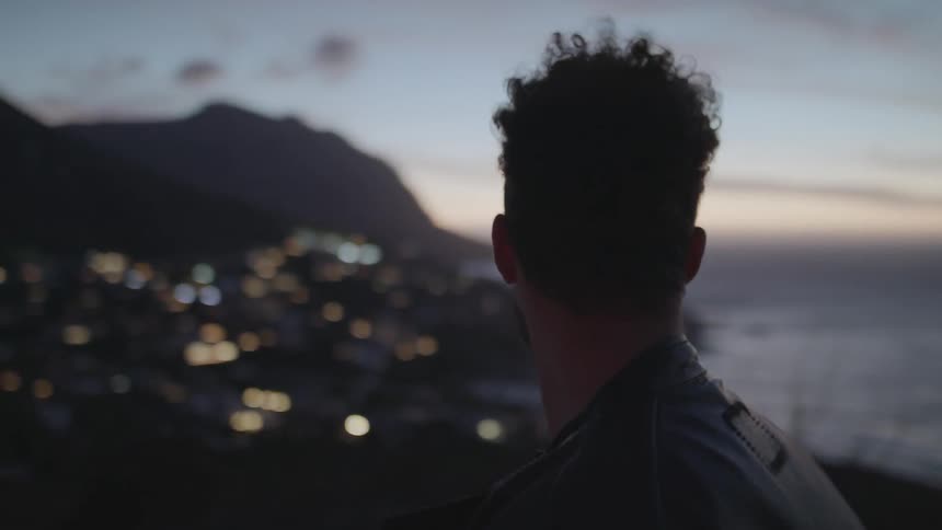 Man standing on a hilltop overlooking a city by the water