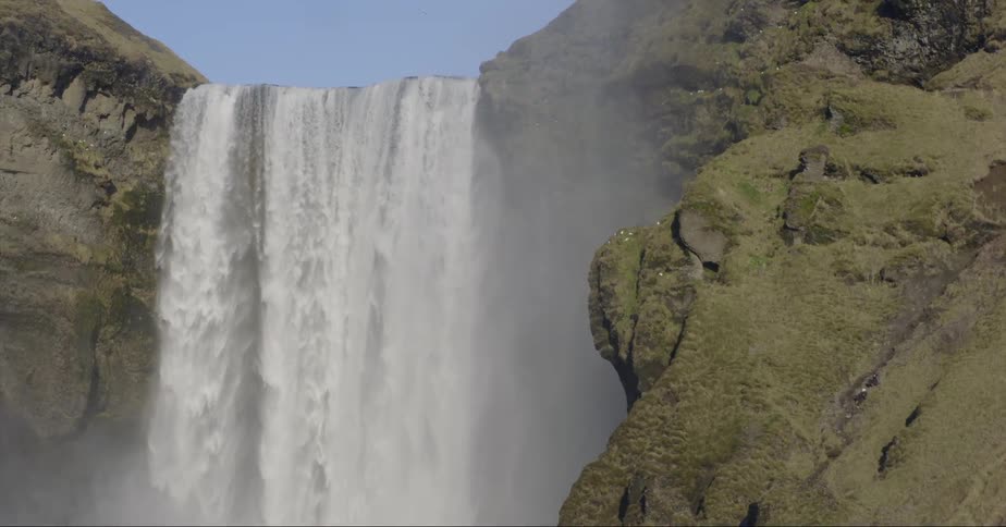 A waterfall flows over a cliff on a sunny day