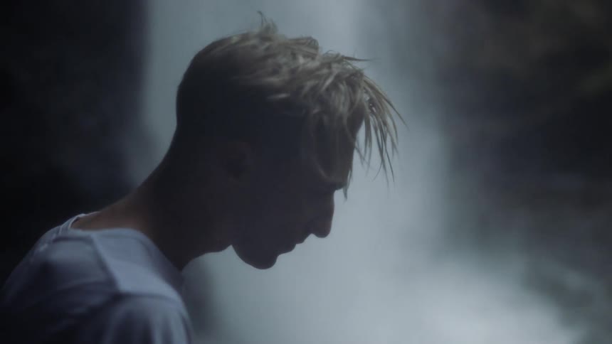 A man is standing with his head down near a waterfall in daylight