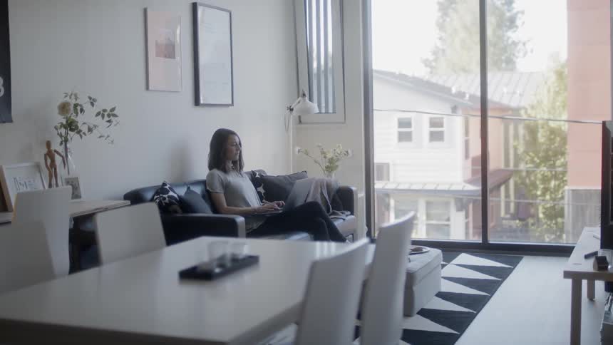 Woman sits on a couch typing on a laptop
