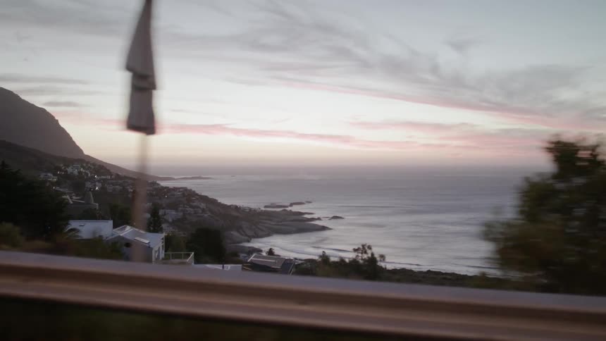 A car drives on a coastal road at sunset