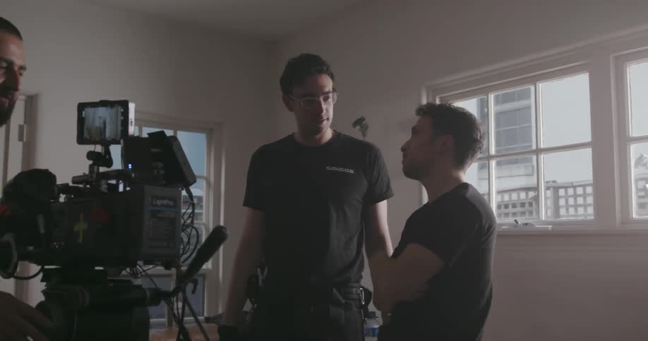 Men talk and gesture near a cameraman and equipment