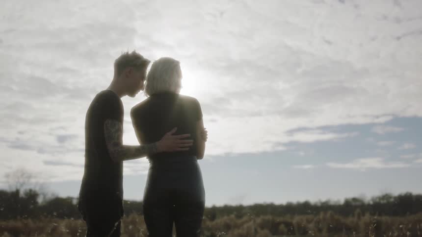 A man is leaning in to hug and comfort a woman as they stand outside in daylight