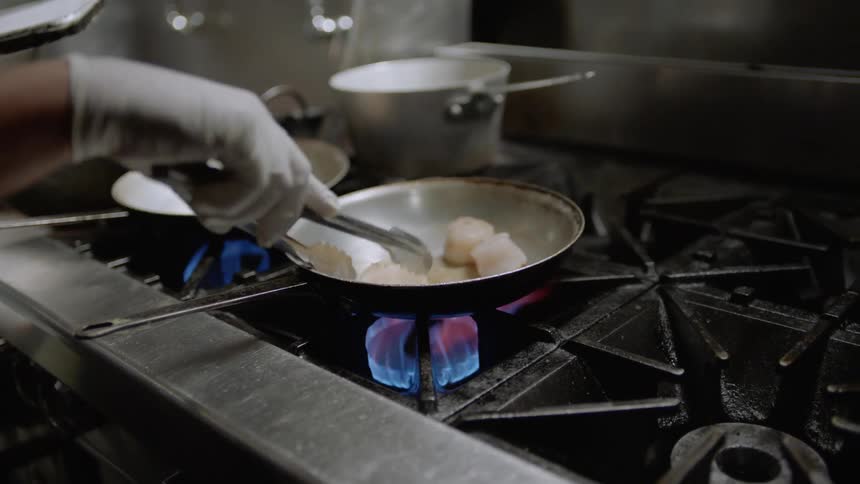 A man cooks scallops in a skillet