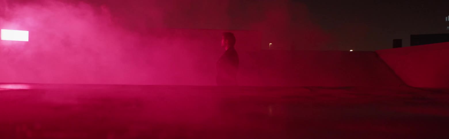 Man stands outside in billowing red smoke at night