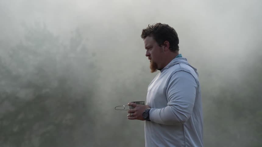 Man holding a mug stands outside on a foggy day