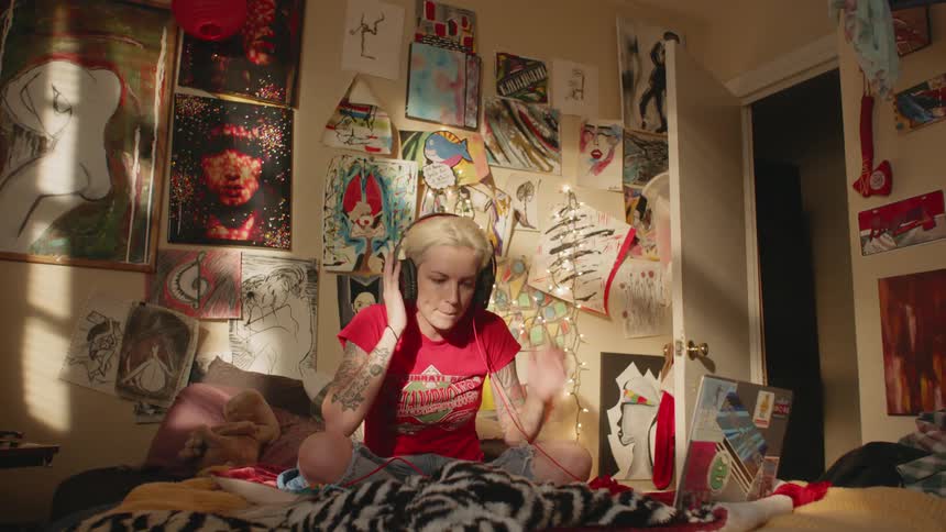 A woman climbs onto her bed and puts on headphones to listen to music