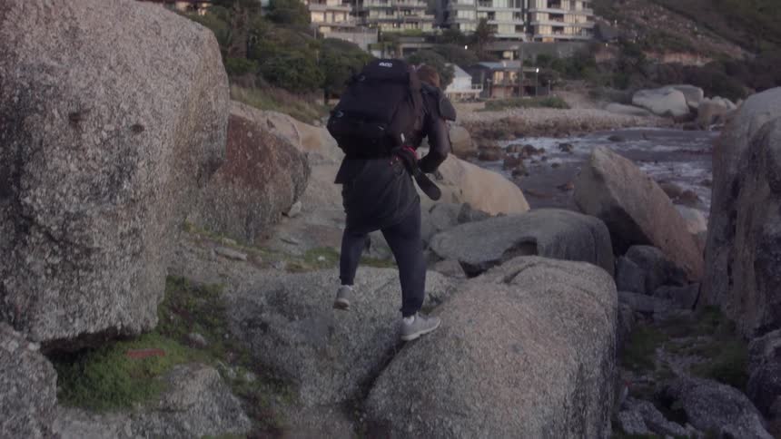 A man climbs up rocks on the shore