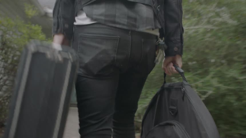 Man carries guitar case and backpack into a house
