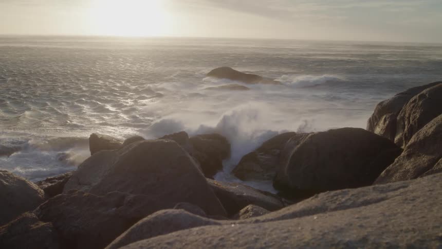Foamy waves crash into the rocks under the bright sun