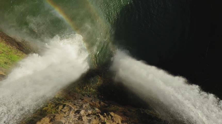 Rainbow reflected in a pool below a waterfall