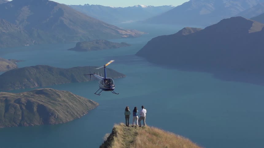A black helicopter hovers in front of three people on the mountains