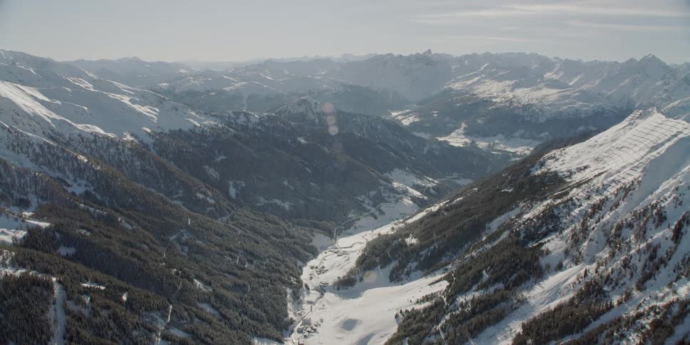 Sun shines over snowy tree covered mountains