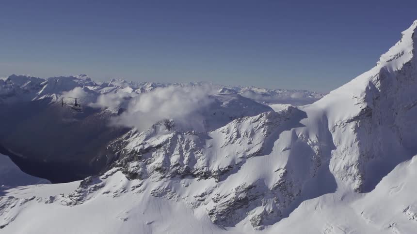 A helicopter flies over snow-covered mountains