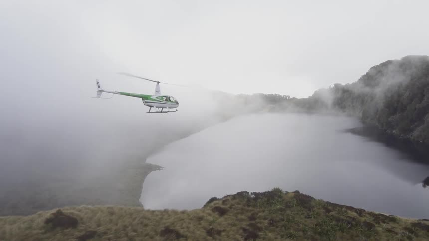 A helicopter flying through the fog and over a mountain lake