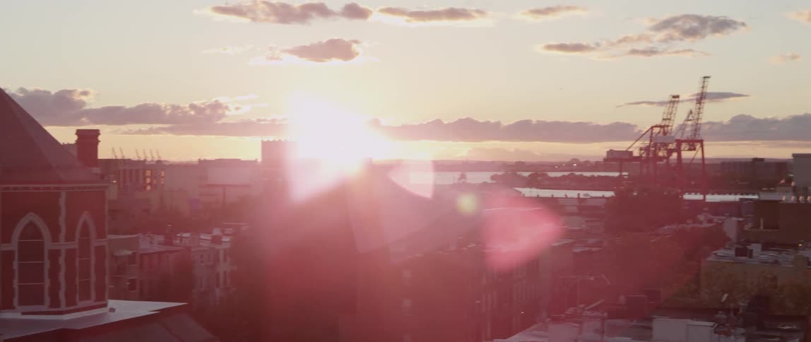 Aerial view of a church, buildings and an industrial area located next to a body of water as the sun glares