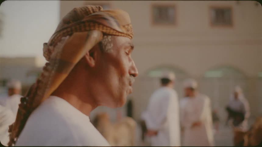 An arab man is talking as he stands in a marketplace on a sunny day
