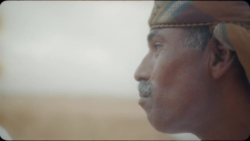 A middle eastern man drinks in the desert