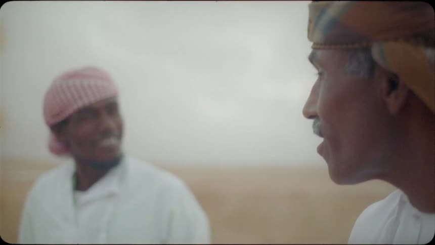 Two middle eastern men eat in the desert